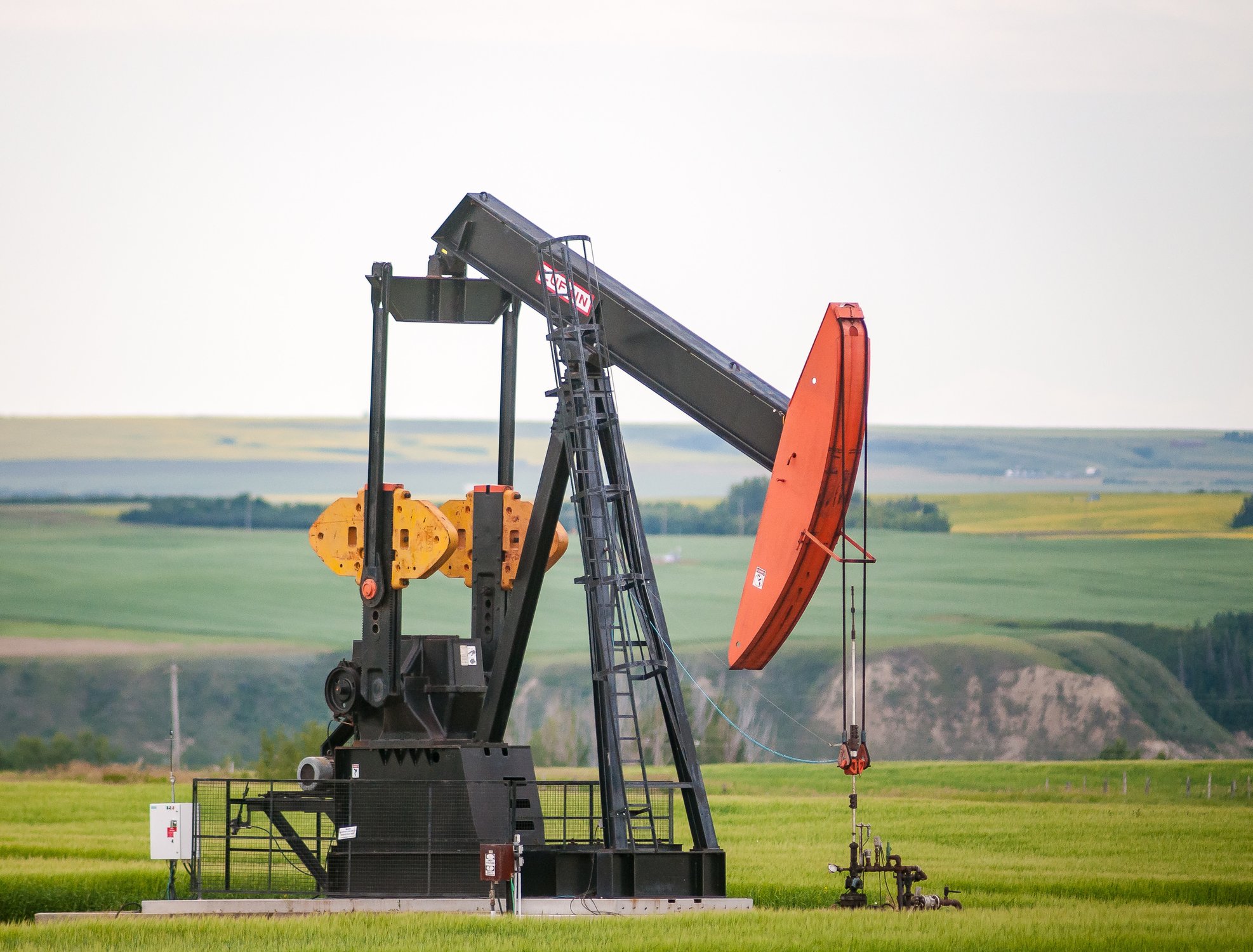 An oil drilling machine with a red top in an open green field