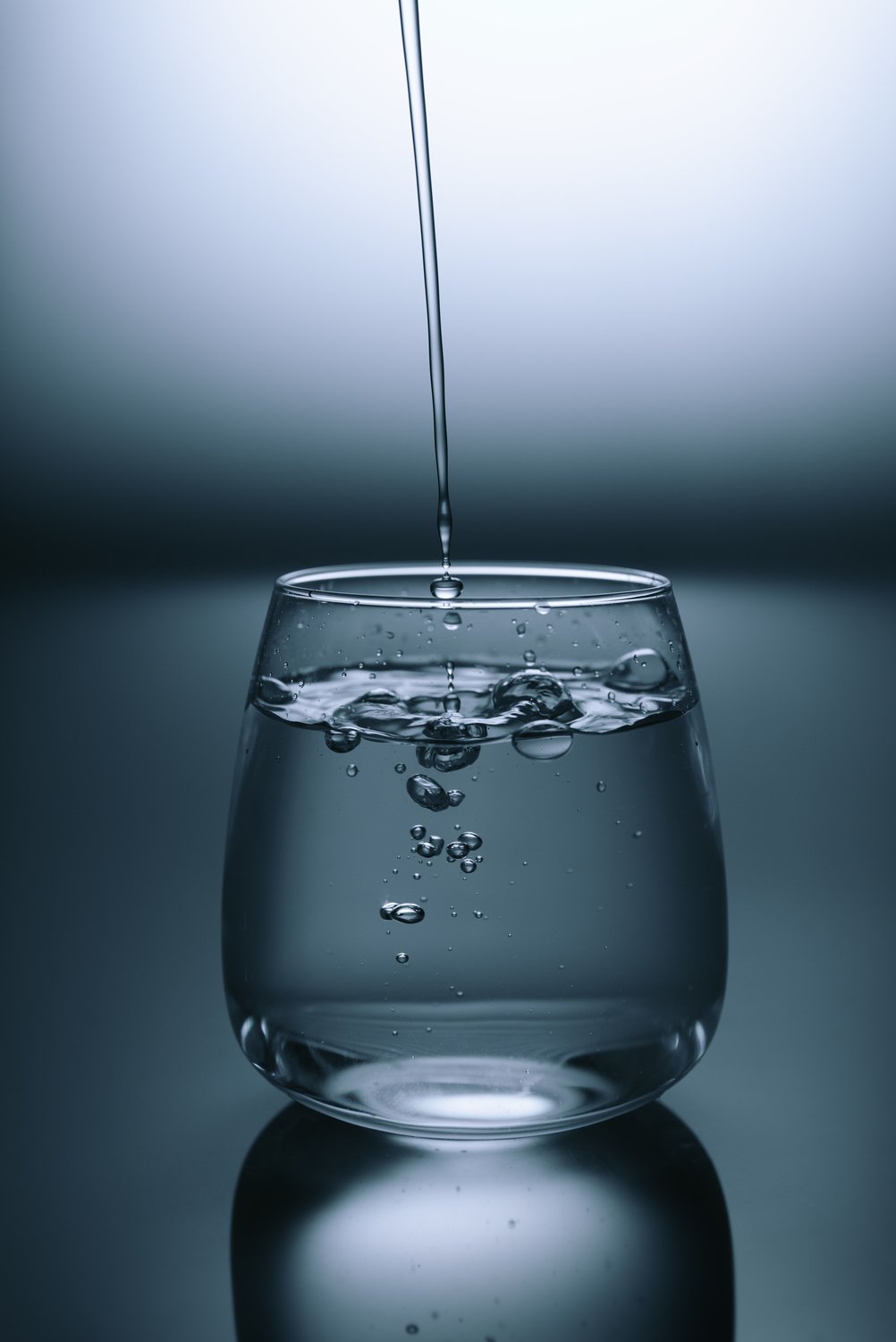 A clear glass being filled from above with water