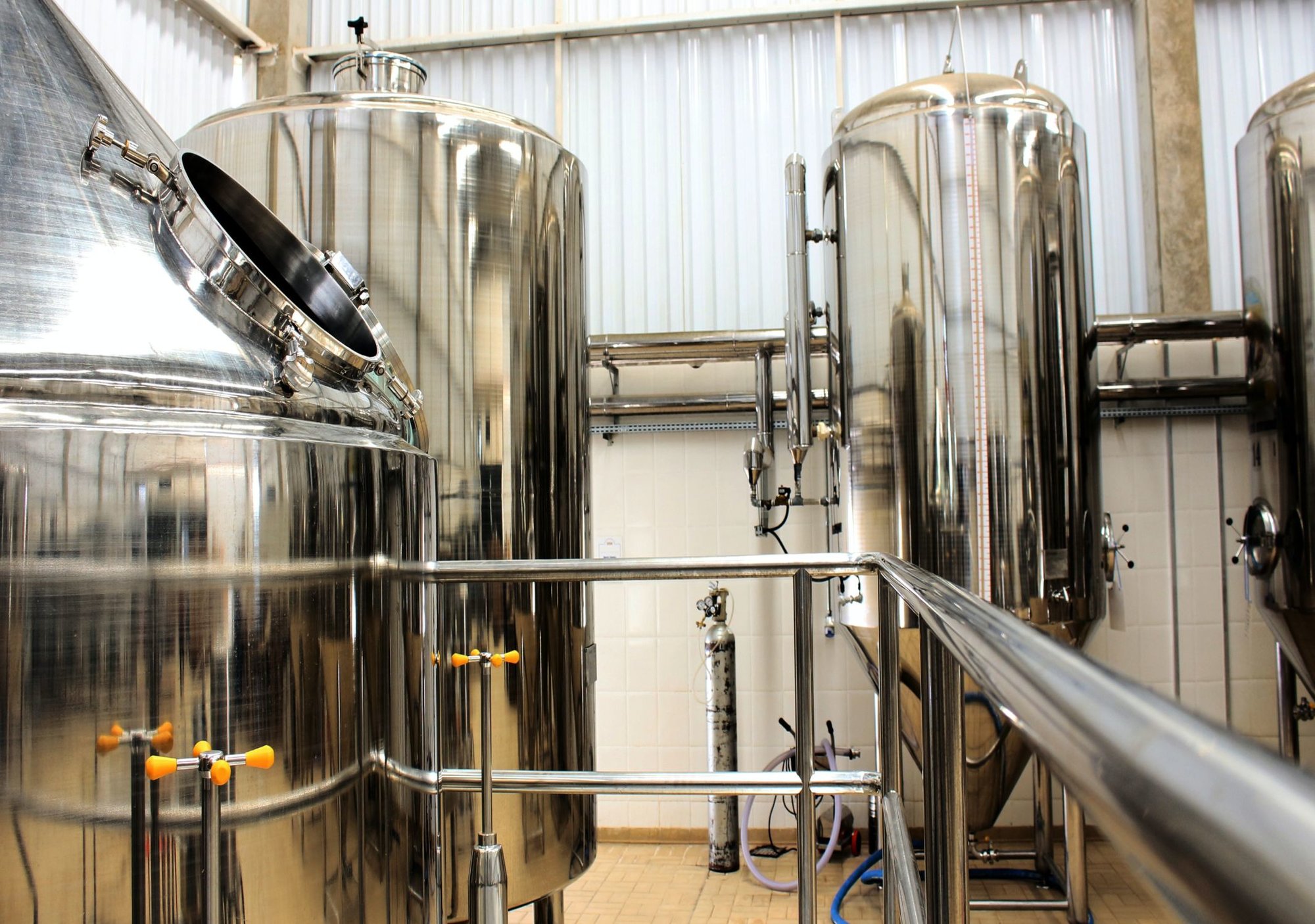 A group of large, shiny silver tanks and boilers in a plant surrounded by metal railings