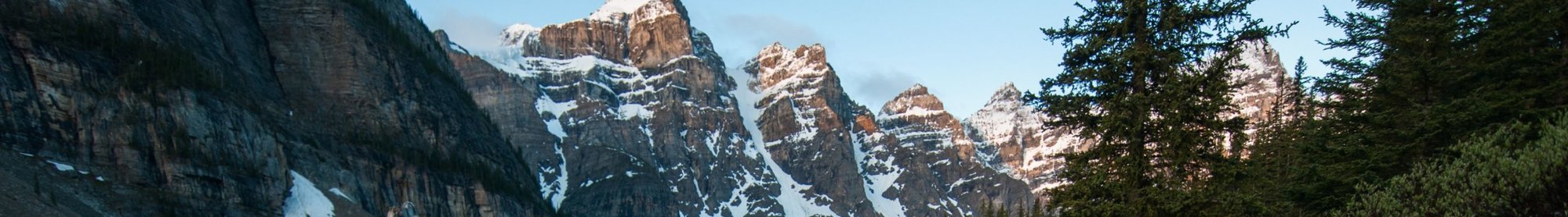 A snow topped mountain range partially shaded with a forest on its edge