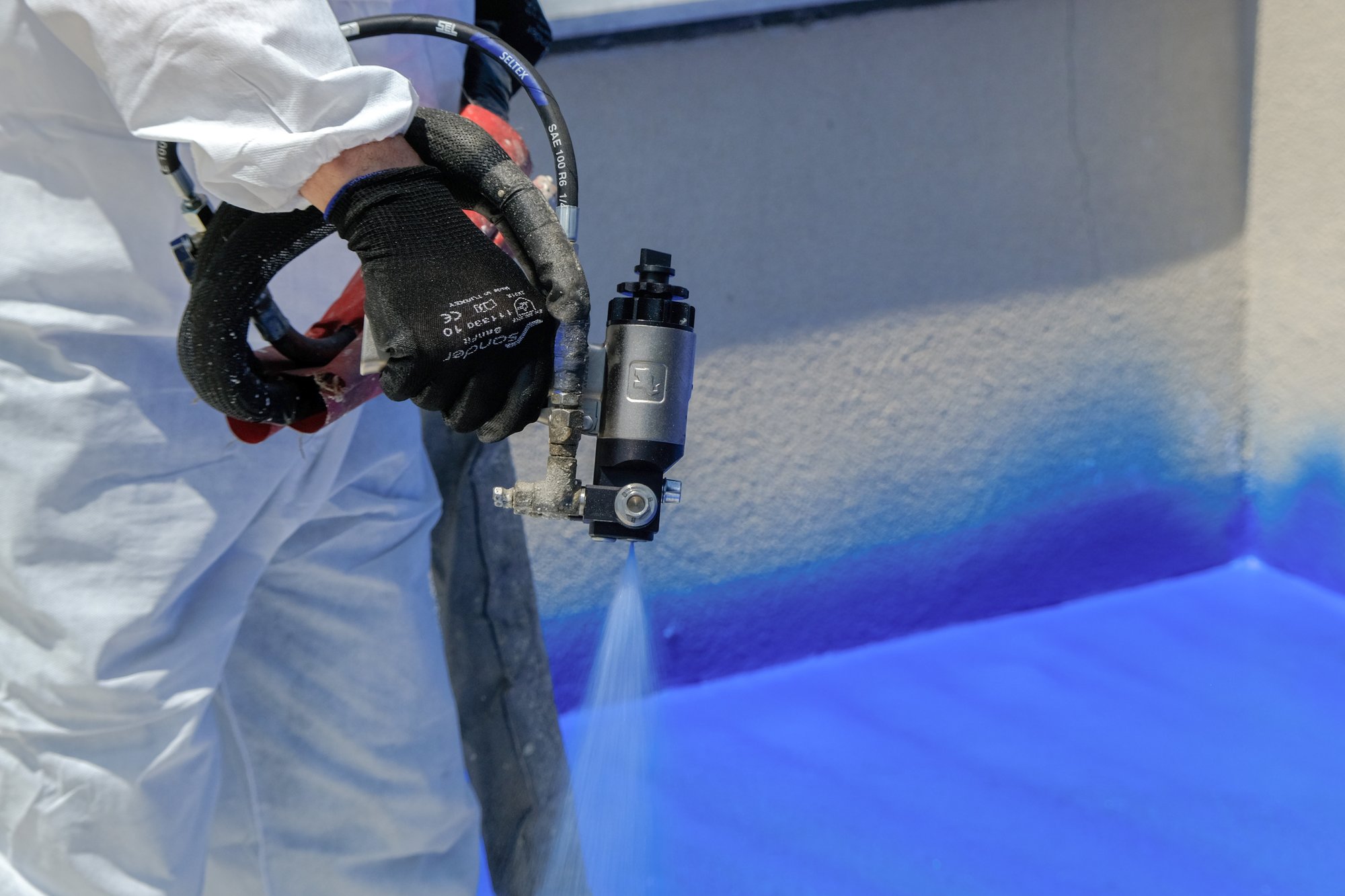 A close up of a black gloved hand holding a sprayer emmitting a blue substance