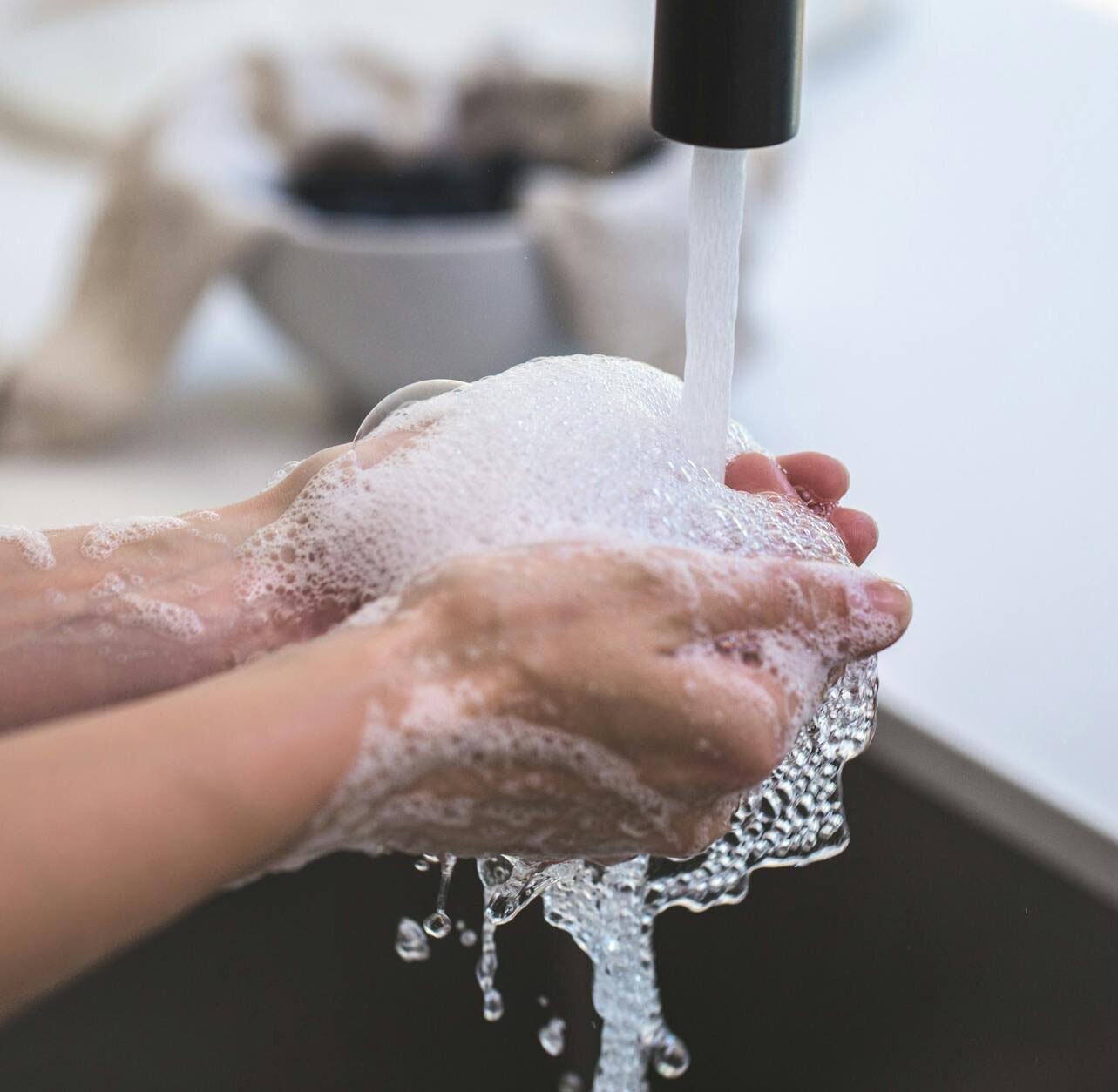 Someone washing their hands under running water, with foaming soap bubbles.