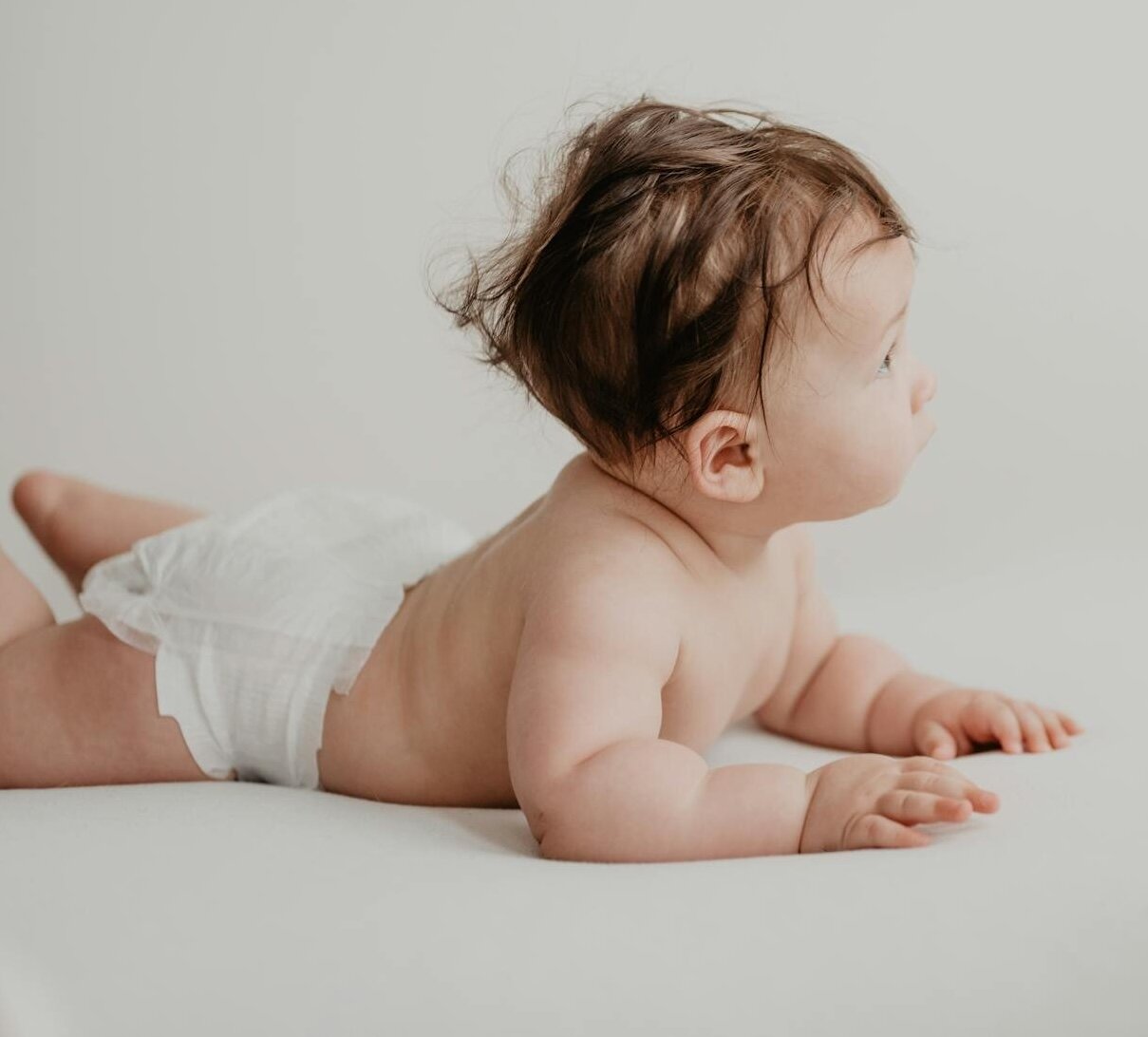 Baby sitting on a white cloth wearing a diaper.