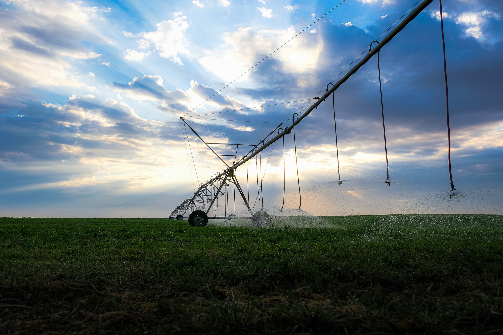 Large metal sprinkler pipes in an open field in front of a cloudy sky