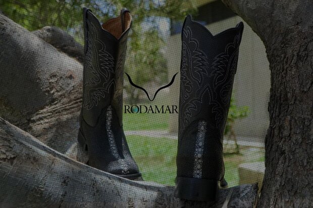 Botas vaqueras de piel negra de la marca Rodamar colocadas sobre una rama de árbol en un entorno natural, destacando como parte de las marcas mexicanas de calzado artesanal.