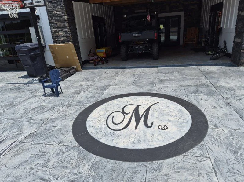 Custom circular monogram medallion set into a gray stamped concrete driveway