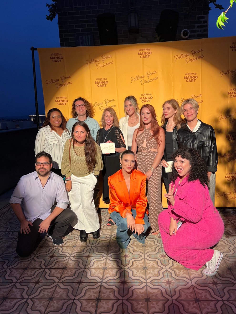Photo of a dozen adults in front of a yellow background posing and smiling at the Follow Your Dreams finale event on Sept. 17, 2023, in Los Angeles hosted by Golden Road Brewing and Mango Cart.