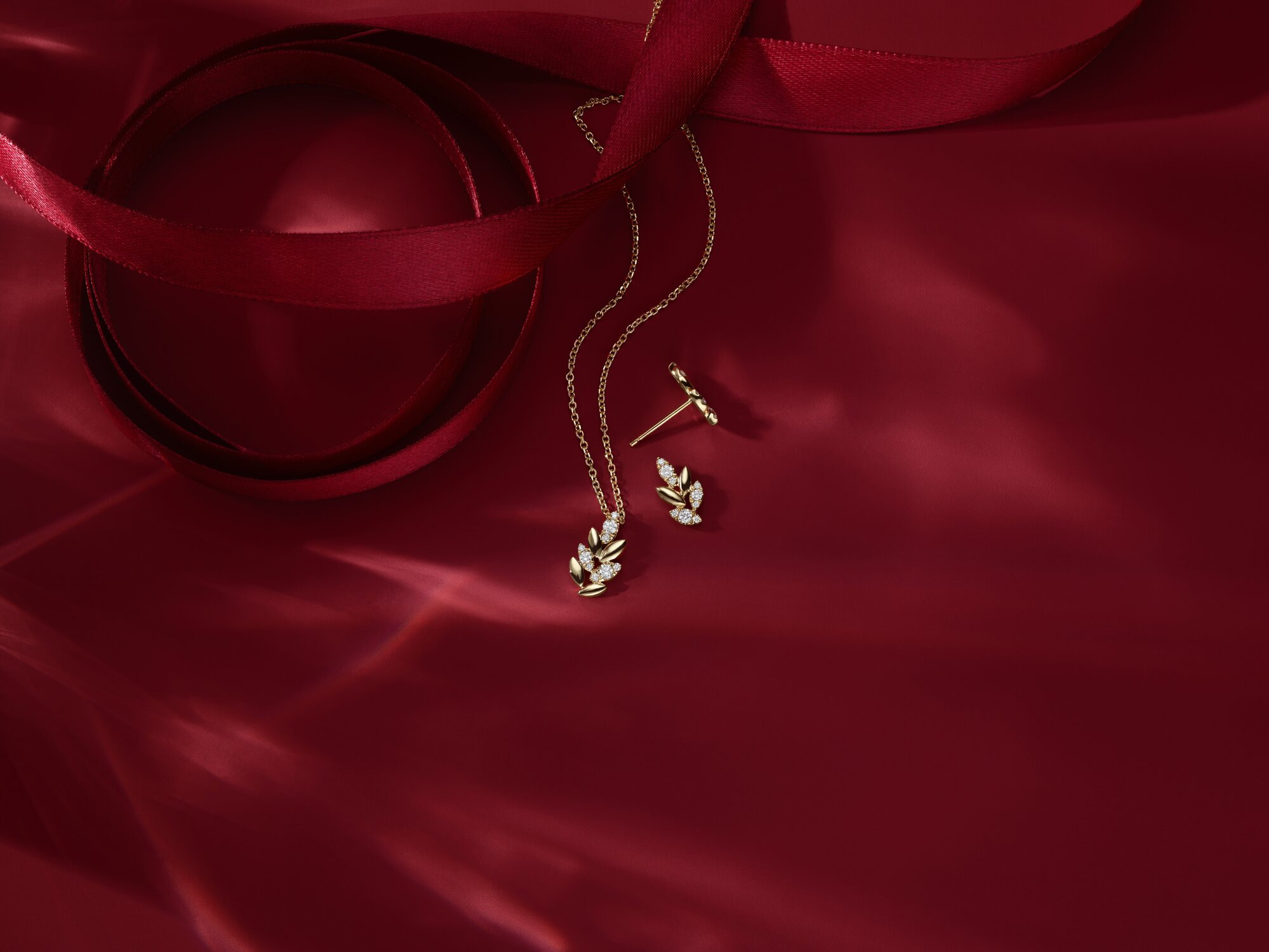 A gold leaf pendant necklace and matching earring with diamond accents on red satin