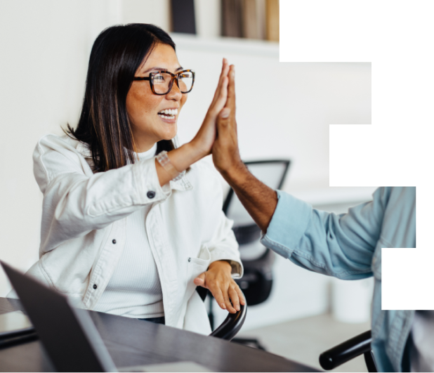 Two coworkers smiling and giving each other a high five in an office setting