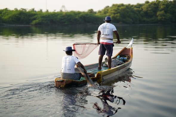 Images shows a gorgeous body of water with two guys on a boat, fishing out more plastic than fish these days, unfortunately. 