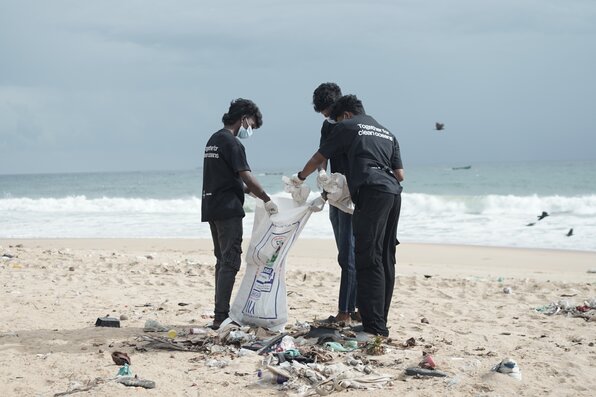 Image shows people on the beach collecting plastic waste and preventing it from polluting the environment.