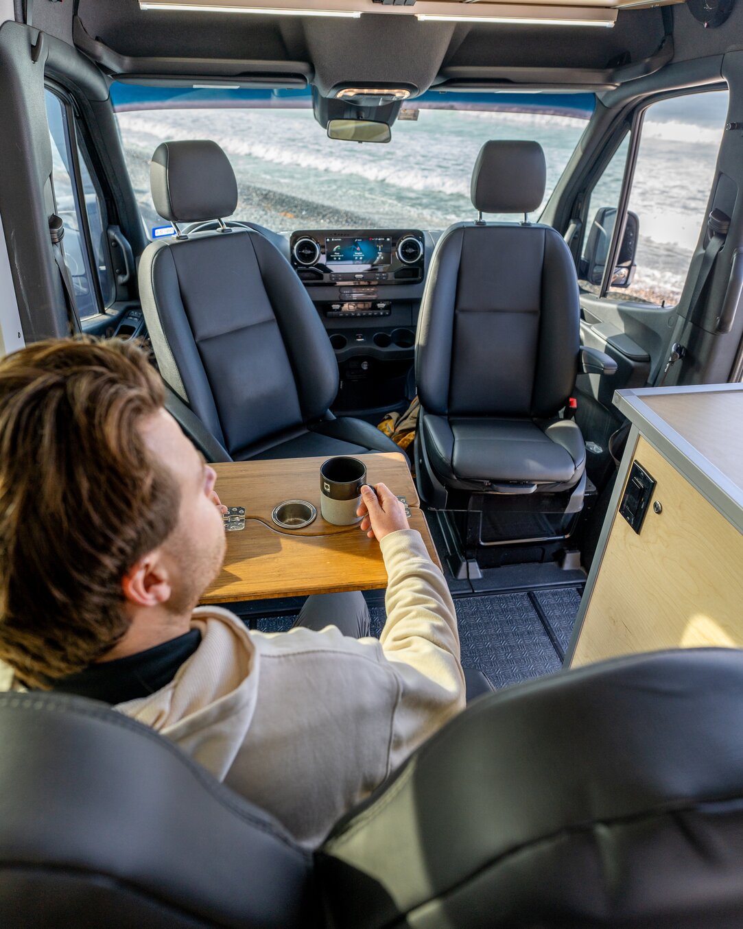 A man is having his morning coffee inside of the 144 conversion van while sitting in the Fenton chair