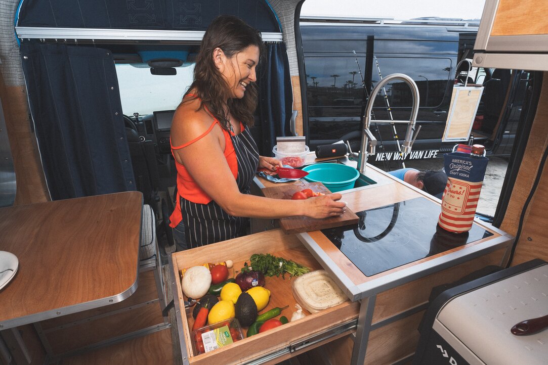 A young lady prepares a meal at the all-in-one kitchen cabinet. She organizes vegetables in the open drawer, uses a cutting board, and utilizes the deep well sink.