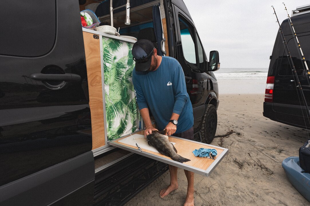 Experience outdoor cooking with the versatile all-in-one kitchen. A young fisherman skillfully cuts up a freshly caught fish on the outdoor table that extends from the backside of the kitchen in the slider door opening.