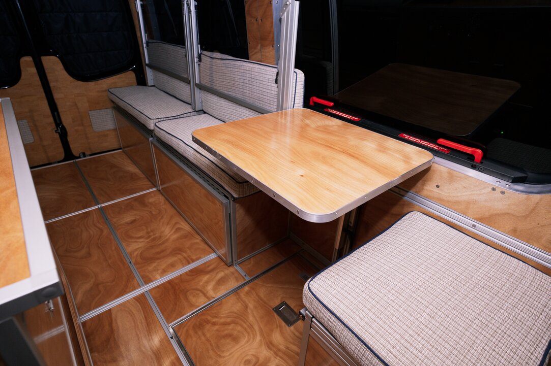Interior of a Sprinter 144 camper van. Cushions with custom blue welt, including the dining table with aluminum edge trim wrap, in the conversion van.
