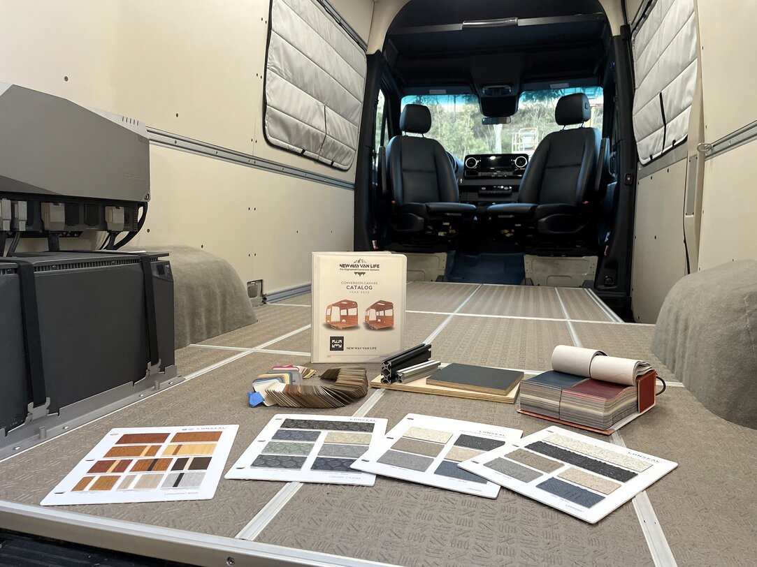 2 people inside of camper van having a conversation around a wall mounted fold down desk while sitting on sectional