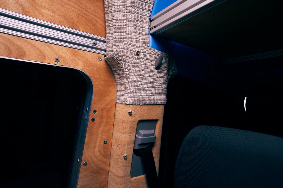 Interior and cockpit of the build showcasing materials used in the conversion van: window frame trim rings, clear-coated African Okoume, plaid fabric wrap, cork-wrapped B pillar, and custom-wrapped headliner shelf. Aluminum extrusions feature a headliner shelf lip.