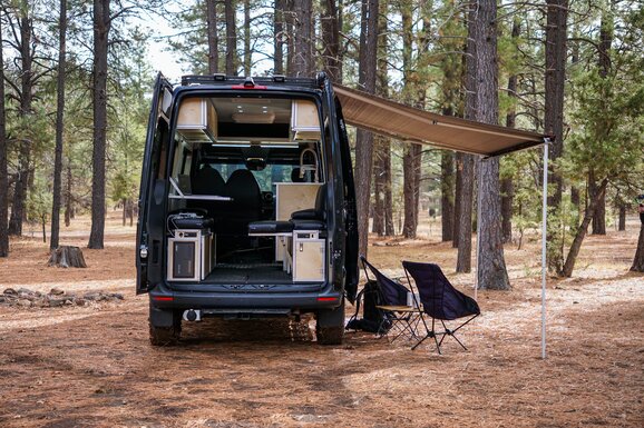 A woman enjoying a morning in her camper van kitchen, pouring coffee while admiring the ocean view. Experience serenity and convenience in our camper van.