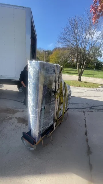Wrapped furniture secured to a moving dolly beside the truck