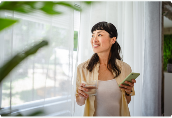A woman standing in a sunlit room, smiling and looking relaxed.
