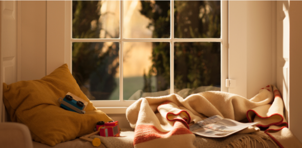 Toy cars and a folded newspaper lying on a neatly made bed near a sunlit window.