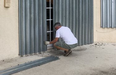 A homeowner boards up their home’s windows and doors in preparation for a storm