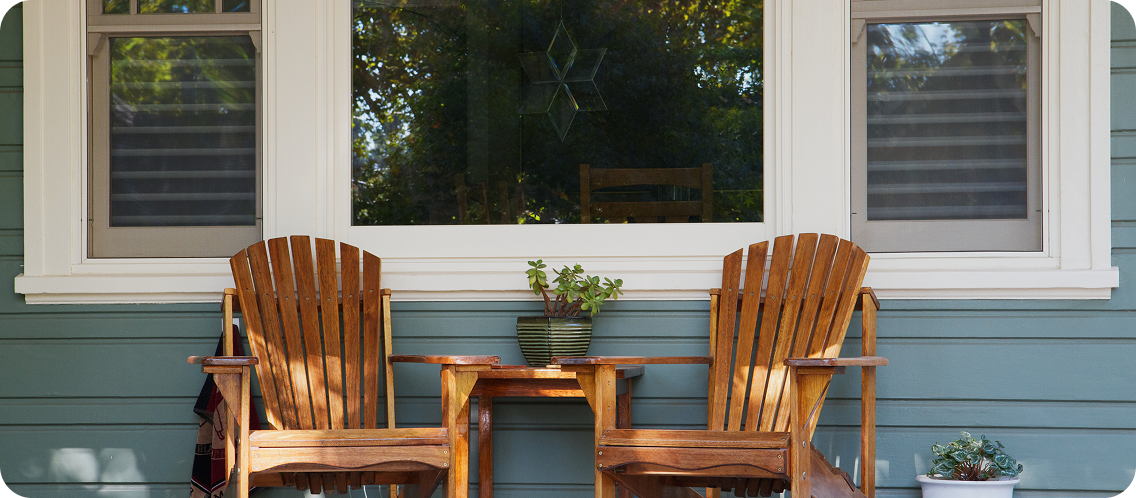 Two wooden Adirondack chairs on a home's front porch.