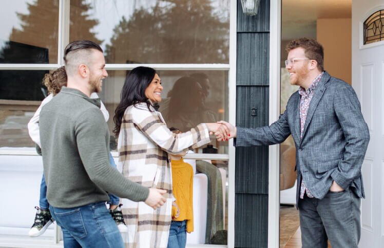 Couple greeting a real estate agent with a handshake outside a home, symbolizing house showing, buying, or selling process.
