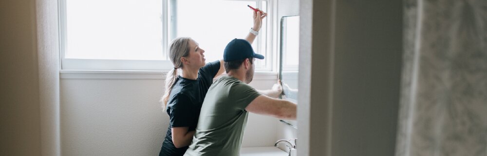 Two homeowners work together to hang a mirror above a sink in a bathroom