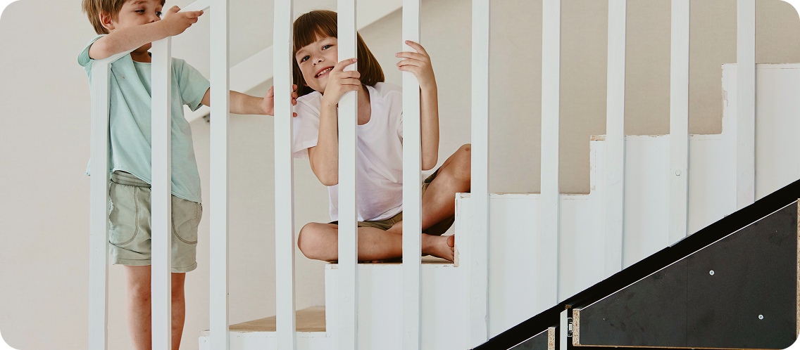 Two children playing on a staircase railing inside a home.
