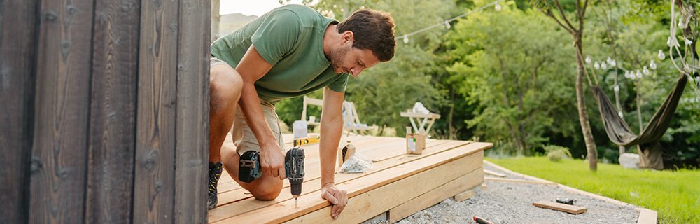 A homeowner uses an electric drill to help build a deck for their backyard. 