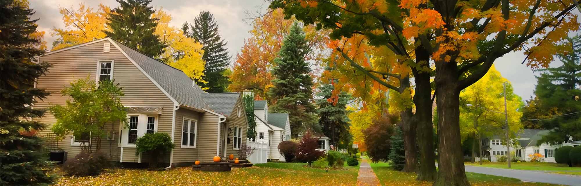 A residential neighborhood is surrounded by trees with leaves changing color during the fall season.