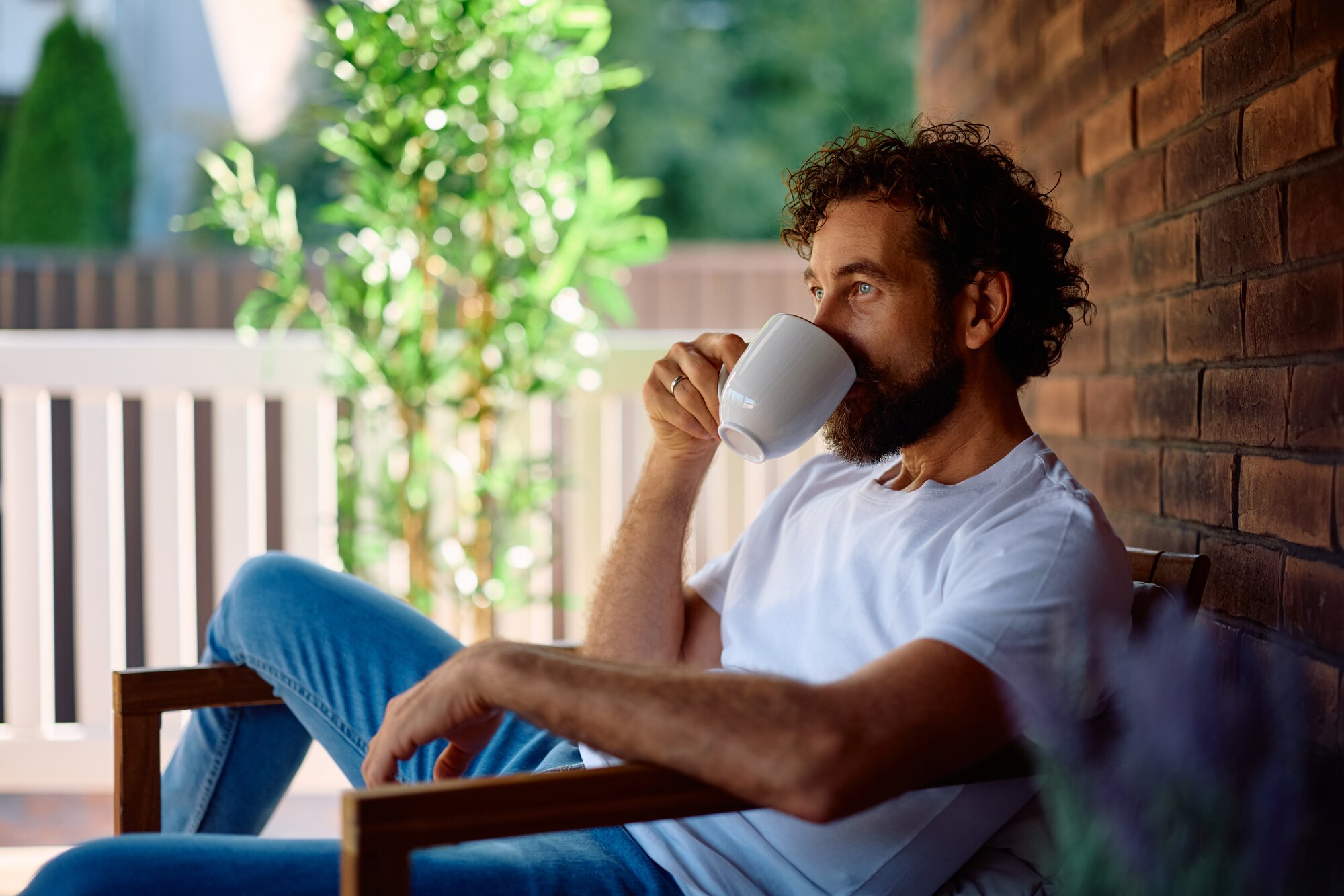 A man sitting outdoors, drinking from a cup.