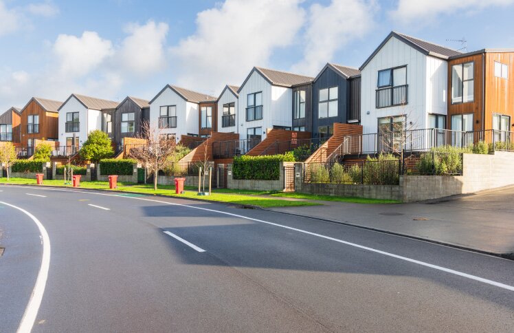 A row of modern suburban townhouses with varied facades and small front yards under a partly cloudy sky.