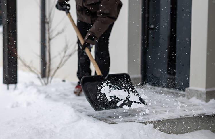 A homeowner shovels ice and snow off his front porch. His porch is surrounded by a thick layer of snow.