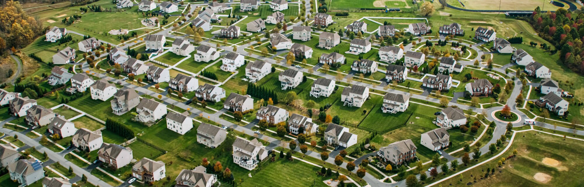 Aerial view of a suburban neighborhood with many homes, green lawns, and winding streets.