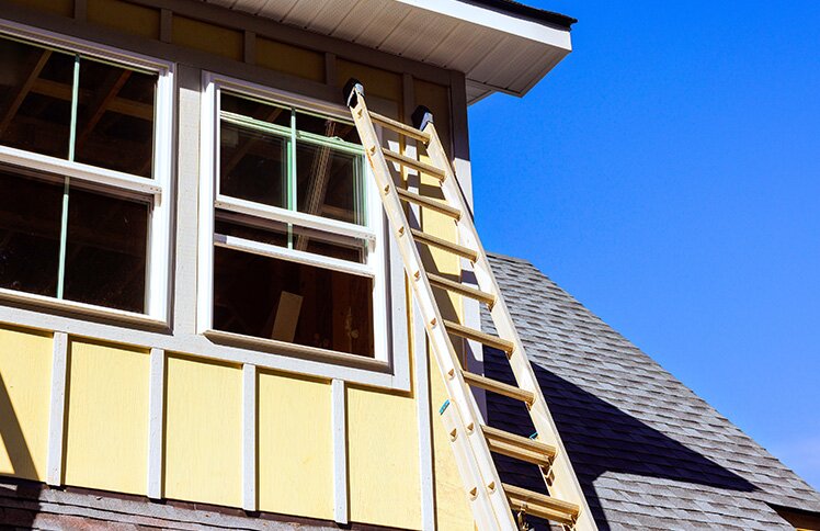 A ladder leans against the second story of a home. The home is under repair.