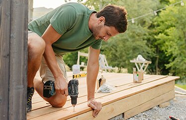 A homeowner uses an electric drill to help build a deck for their backyard. 