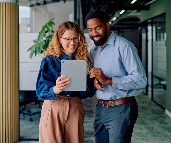 Two colleagues smiling and talking in a bright office environment.