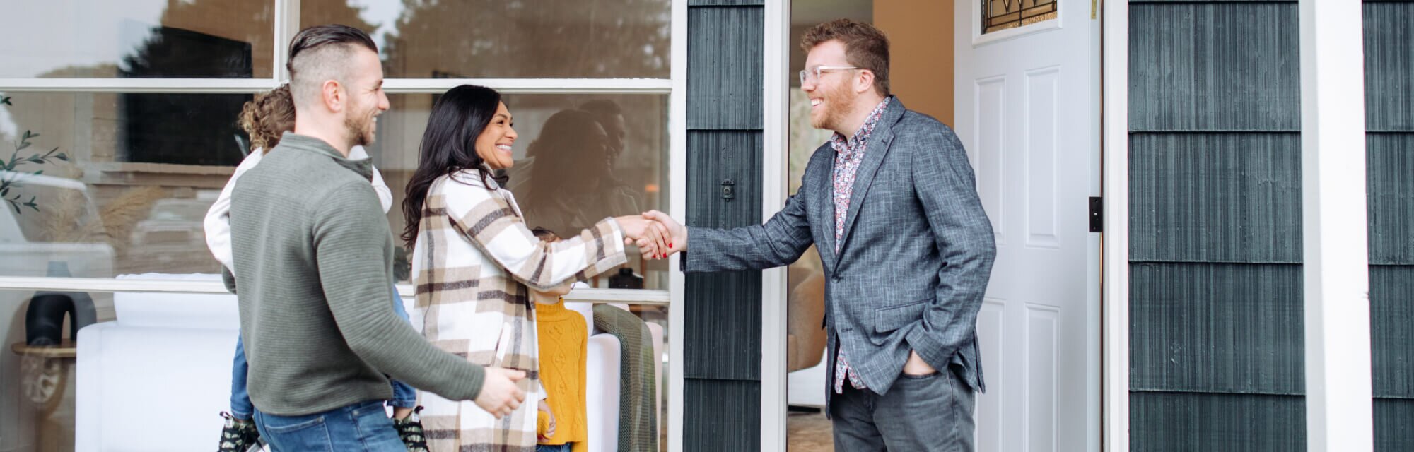 Couple greeting a real estate agent with a handshake outside a home, symbolizing house showing, buying, or selling process.