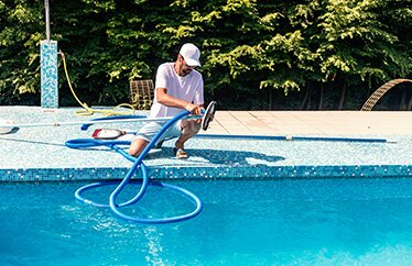 A homeowner performs preventative maintenance on their pool during a sunny day. 