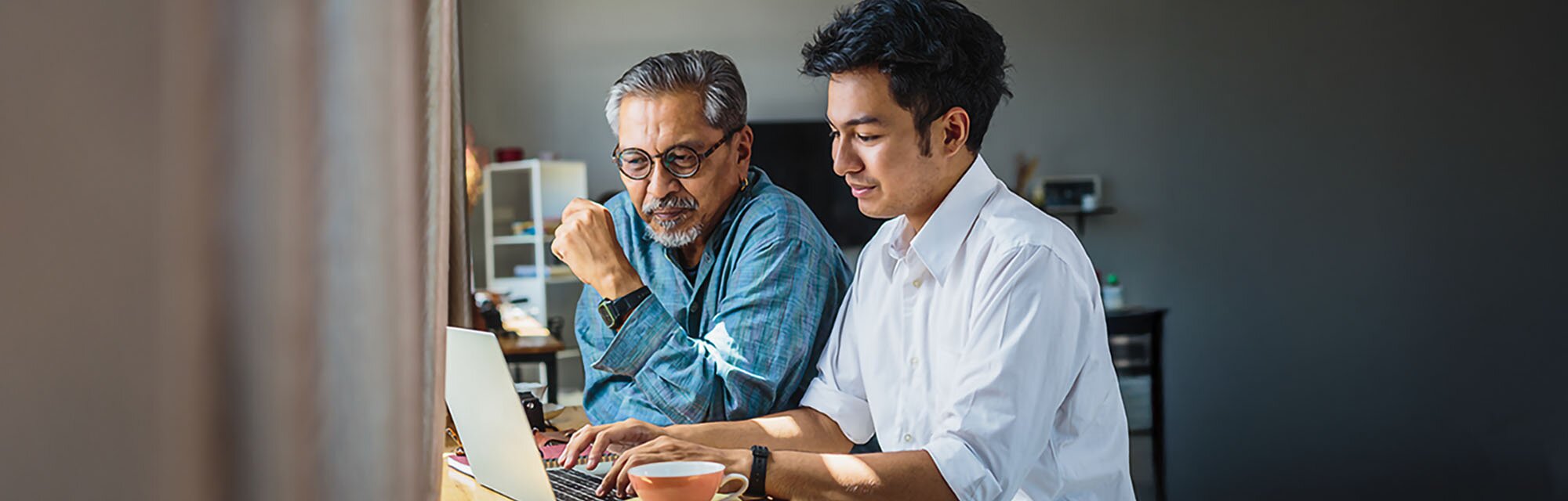 A young man and his older relative review something on a laptop together.