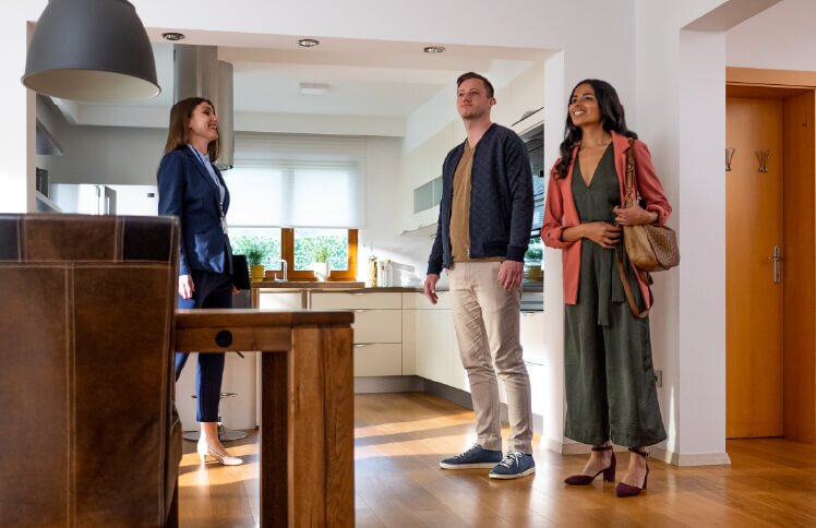 Two homebuyers view a home’s kitchen with their real estate agent while considering the best time to buy a house.