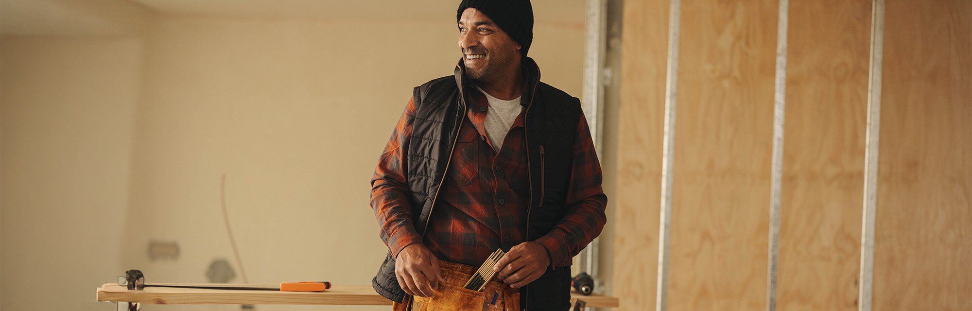  A homebuilder wearing a toolbelt stands smiling in a new construction home.