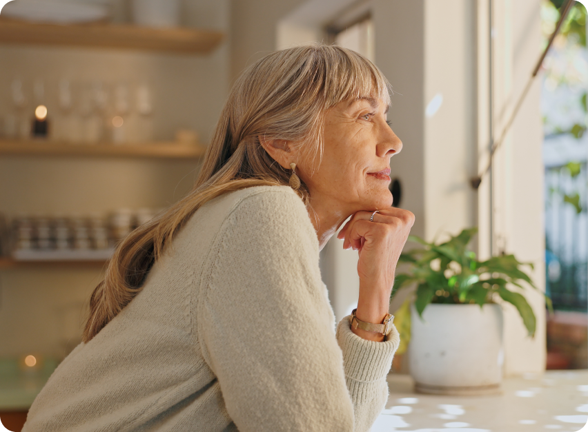 A woman sitting by a window, looking thoughtfully into the distance.