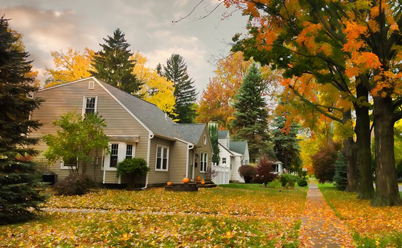 A residential neighborhood is surrounded by trees with leaves changing color during the fall season.