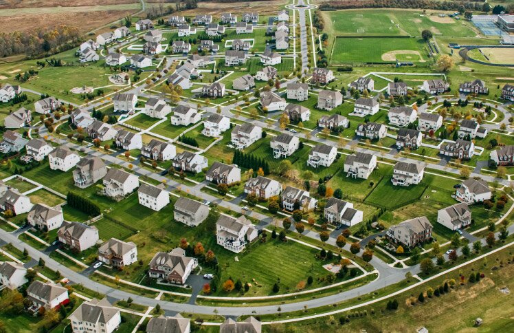 Aerial view of a suburban neighborhood with many homes, green lawns, and winding streets.