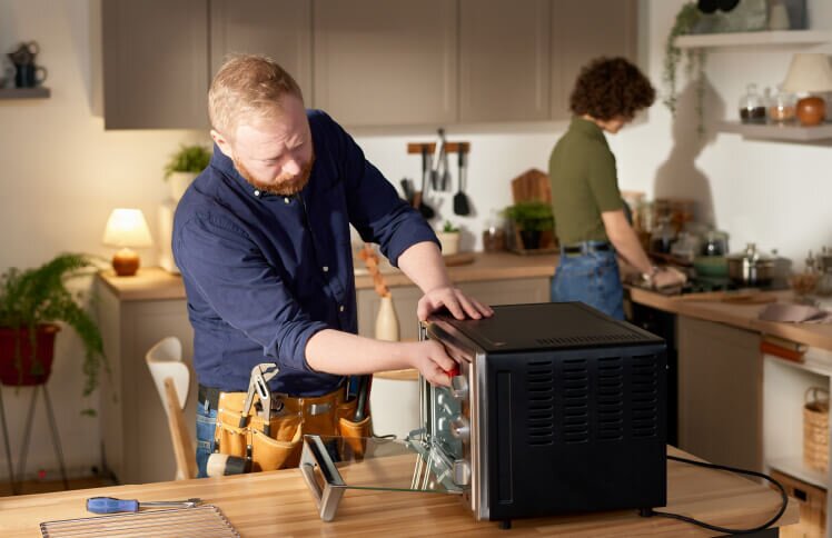 A homeowner in a kitchen completes maintenance on a toaster oven sitting on the counter.
