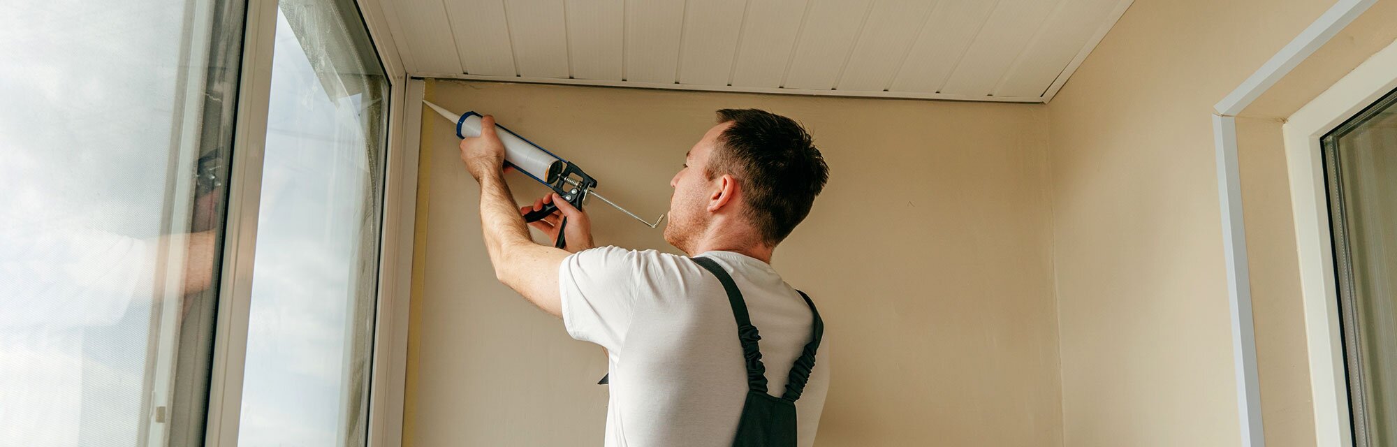 A homeowner re-applies caulk around the windows in his enclosed porch.