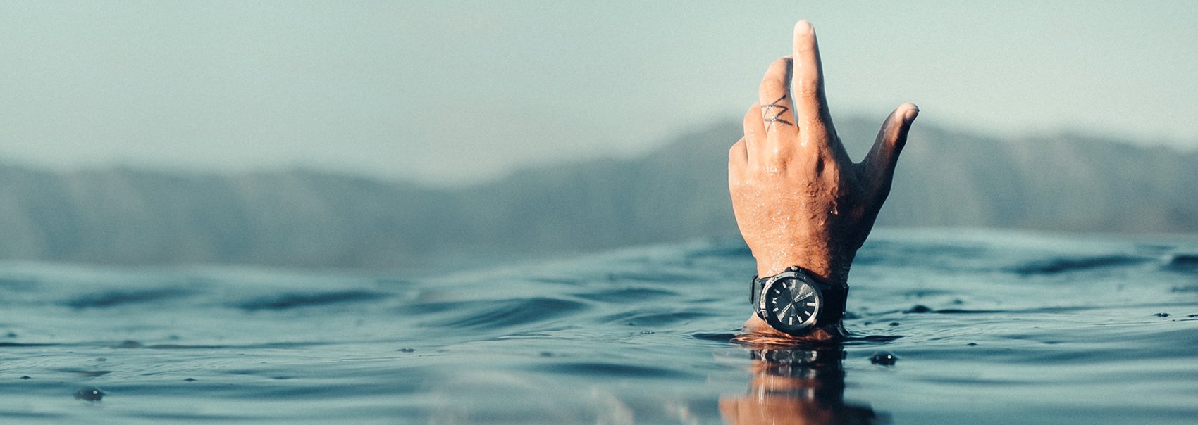 Hand coming out of the ocean with a MVMT watch on wrist